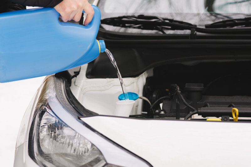 Car maintenance. Man pouring car winter windshield washer fluid outdoor. Closeup image taken outdoors.